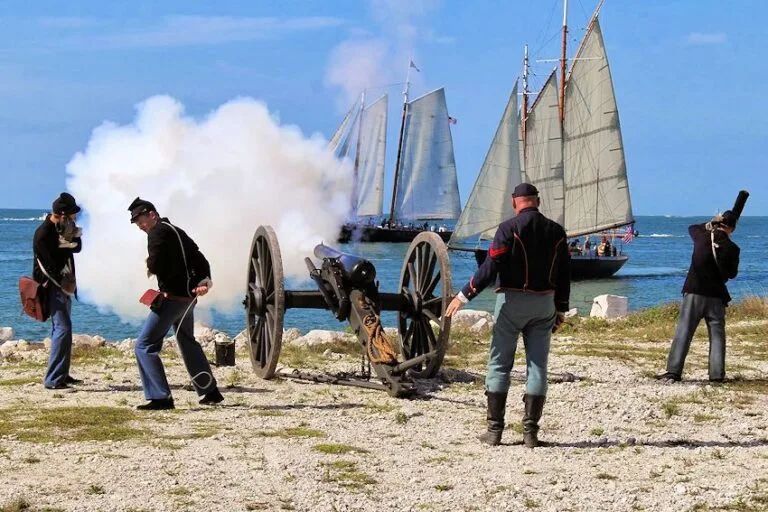 Historic cannon firing on Key West shoreline with tall-ship sails in background, popular scene for Key West boat tours and sandbar charters