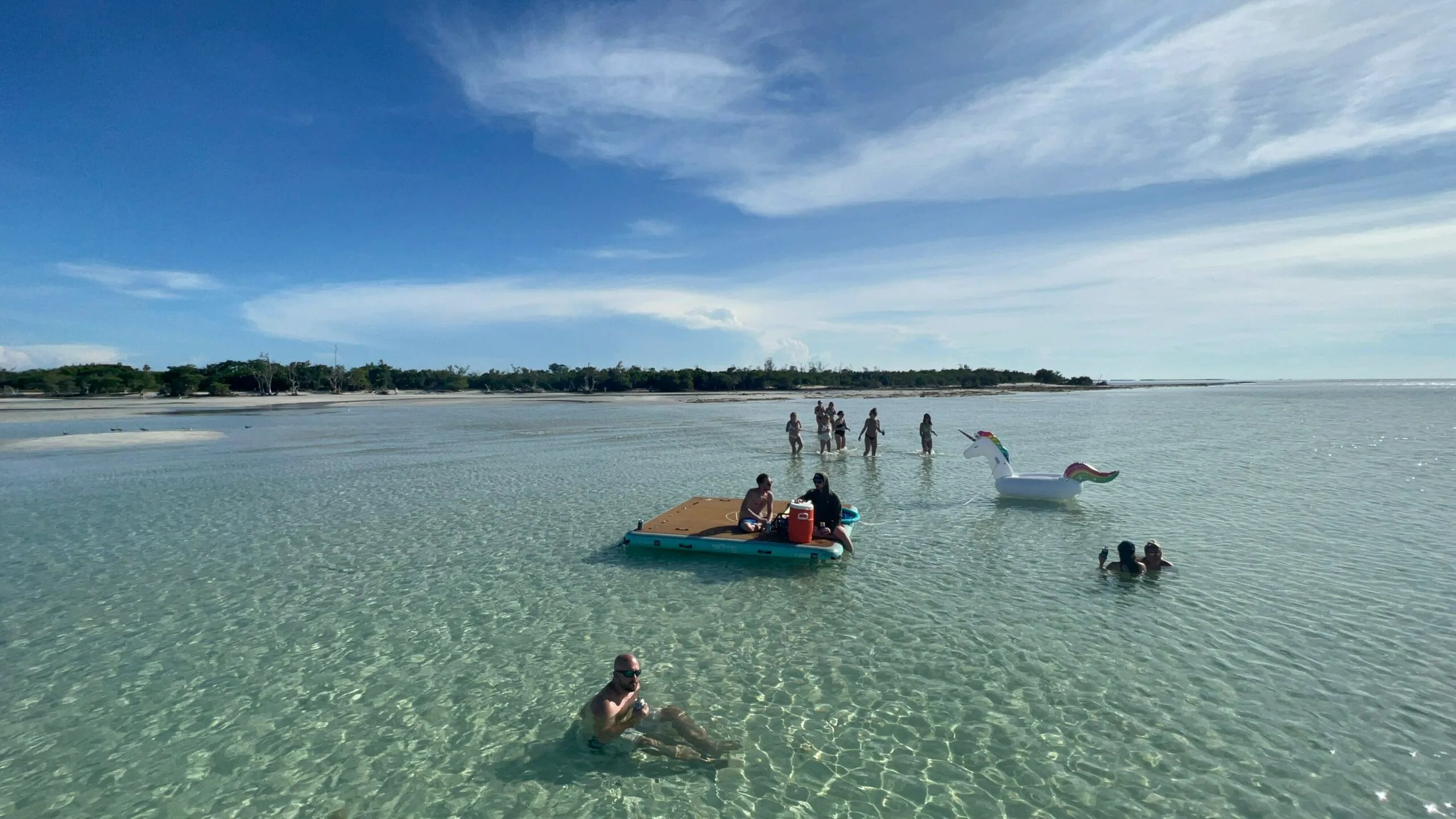 Shallow turquoise Key West sandbar with swimmers, inflatable unicorn and a small floating dock—popular spot for sandbar charters and private boat trips