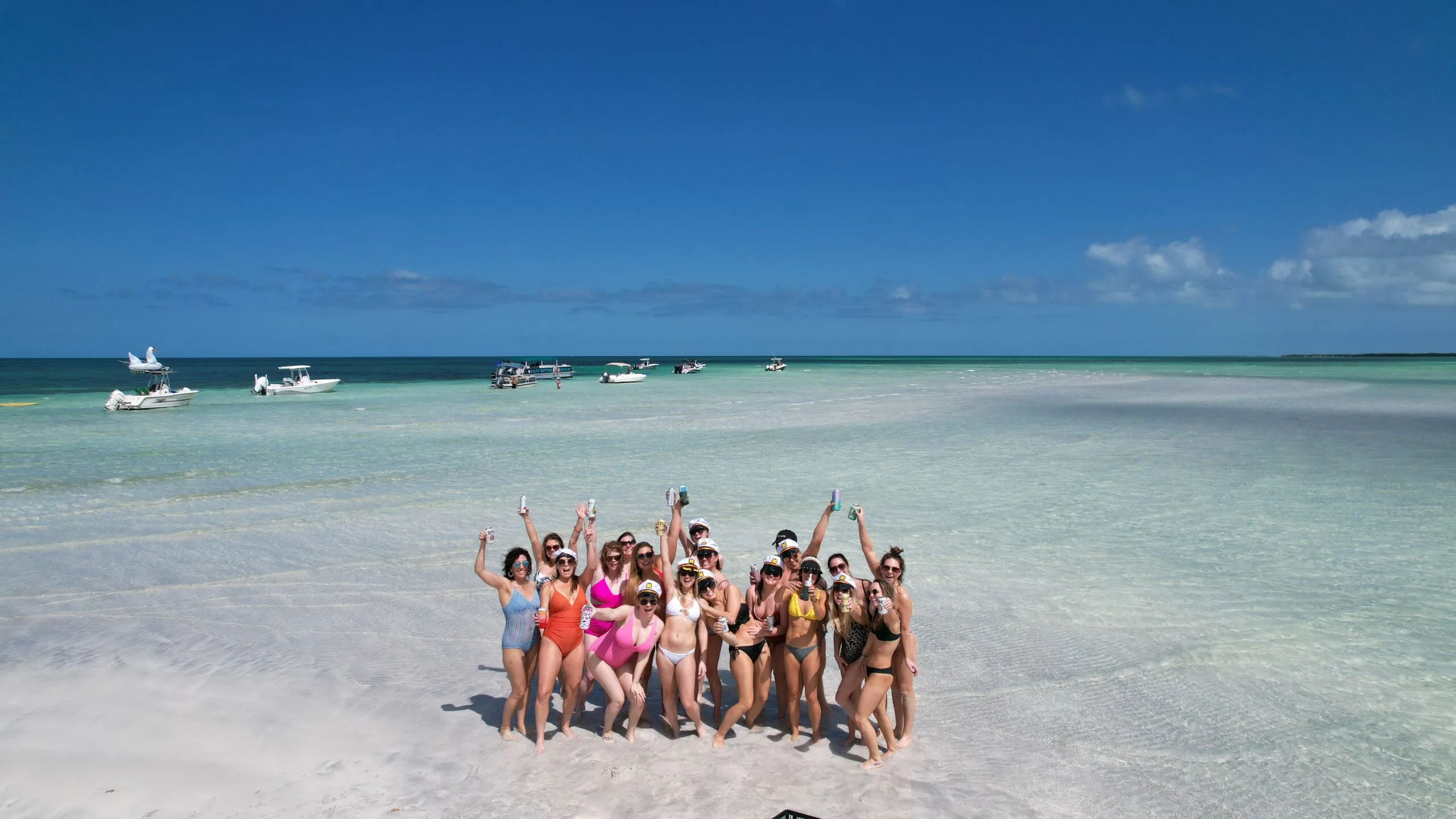 Group celebrating on a shallow Key West sandbar with anchored boats nearby, ideal for sandbar charters and private boat trips.