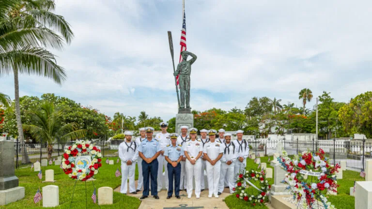 Memorial honoring fallen sailors with military personnel and floral tributes at a Key West naval cemetery.